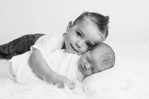 Menifee baby and sibling photographer: Black and white photo of little boy posing with sleeping newborn baby brother.