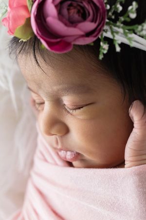 Close-up of sleeping newborn baby girl wrapped in pink swaddle.