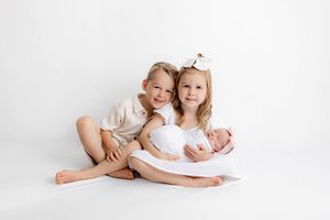 Two siblings holding their swaddled newborn baby brother on white background.