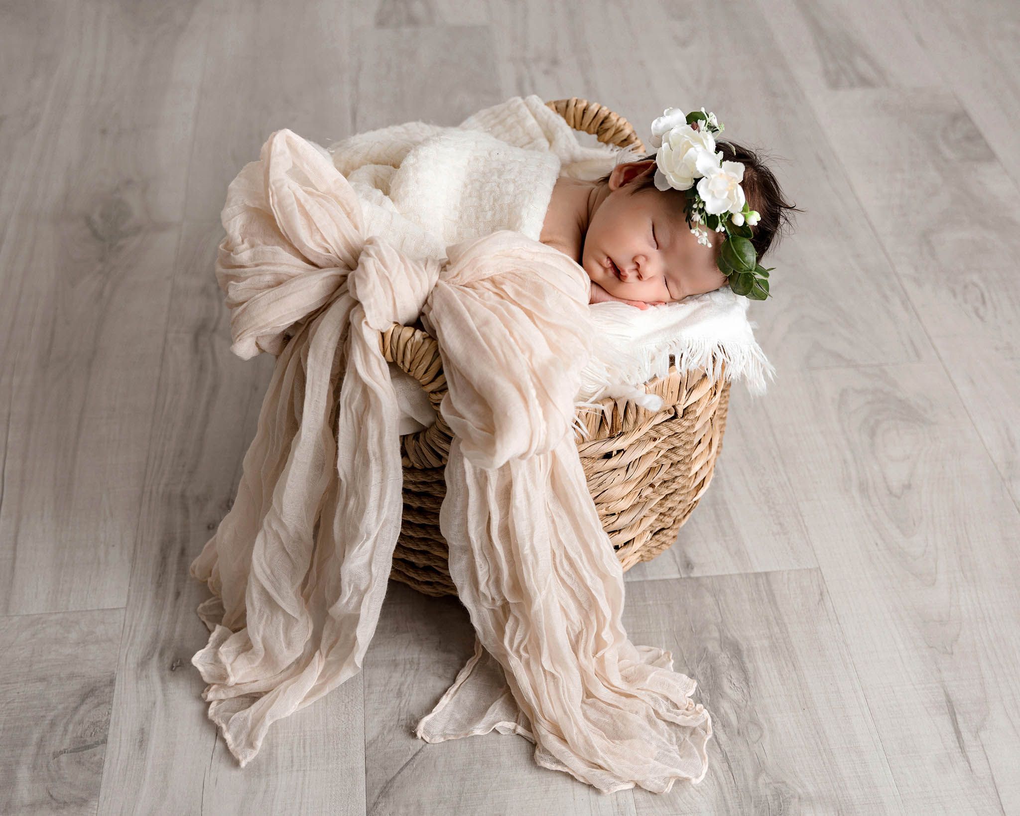 Coquette baby photography: Newborn baby sleeping in basket with floral crown and bow wrap.