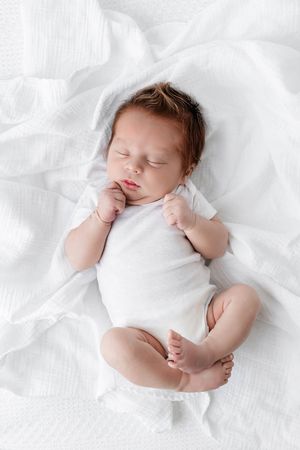 Lifestyle newborn photographer in Menifee: Cute newborn baby sleeping in white onesie on soft white blanket.