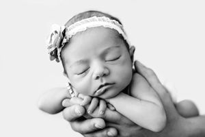 Black and white photo of sleeping newborn baby cradled in parents hands.