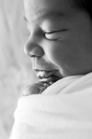 Black and white close-up portrait of a sleeping newborn baby with tiny fingers near face.