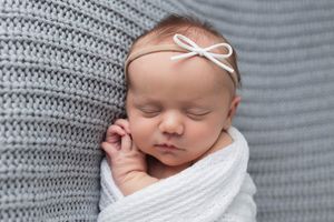 Peaceful sleeping newborn baby girl swaddled in white wrap wearing delicate bow headband.