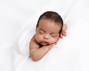 Peaceful sleeping newborn baby with dark hair resting on soft white blanket.