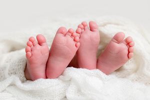 Close-up of newborn twins tiny feet peeking out from a soft white knit blanket, by Menifee baby photographer.