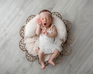 Yawning newborn baby girl in white lace dress lying in a decorative bowl with pink tulle.