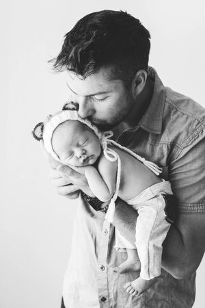 Professional newborn photographer in Temecula: Black and white photo of dad kissing his sleeping newborn baby wearing a bear bonnet.