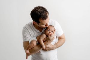 Newborn and family professional photographer in Menifee: Dad kissing his newborn baby boy against a white background.