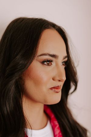 Close-up portrait of a young woman with dark hair, brown eyes, and elegant makeup wearing a red accessory.