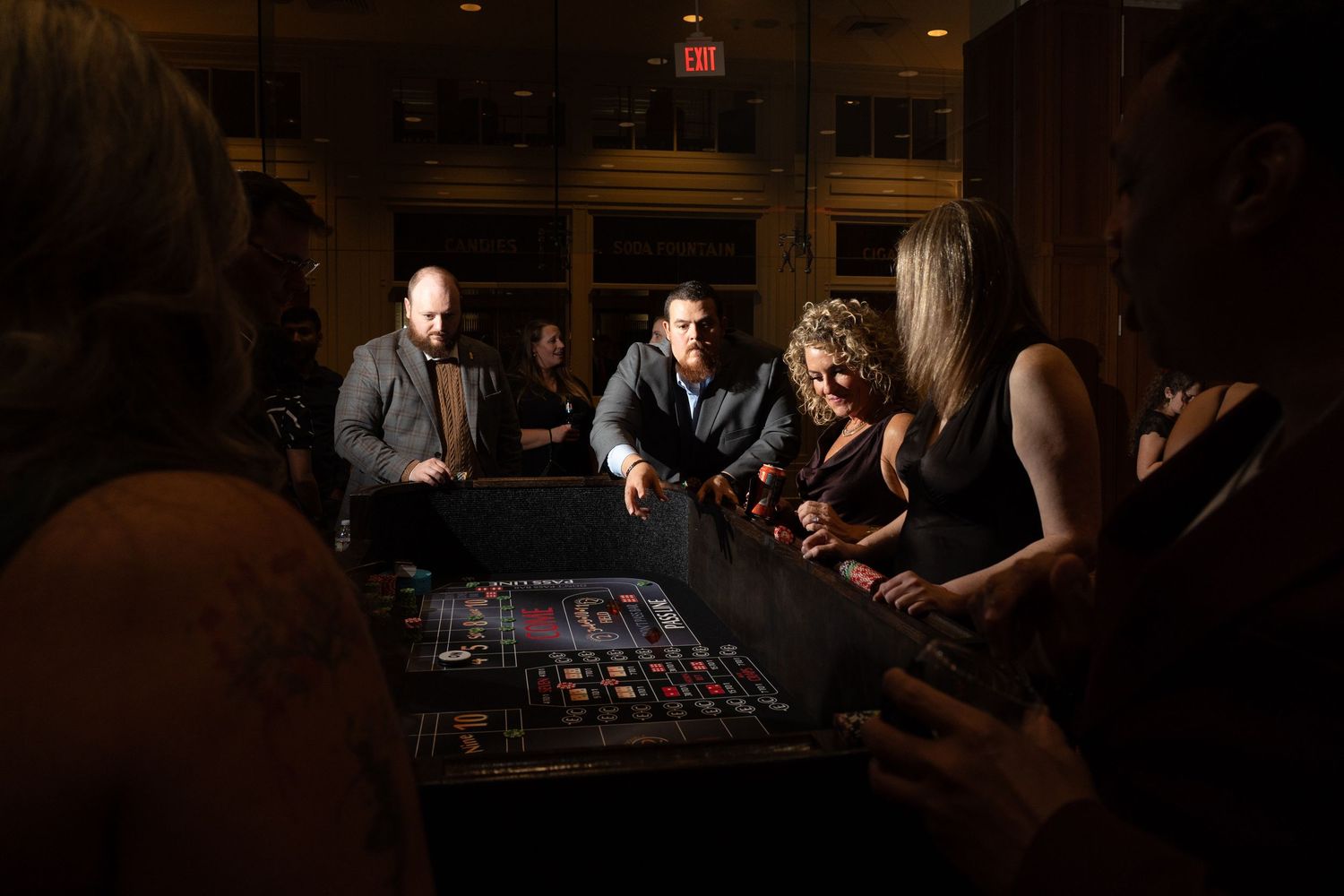 Elegantly dressed guests gather around a casino table in a dimly lit venue during a formal evening holiday party at union station in Dallas.