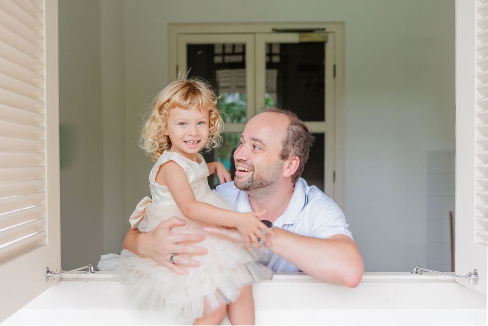 A Relaxed Russian caucasian dad with a laughing blond child in light wooden windowsill in singapore