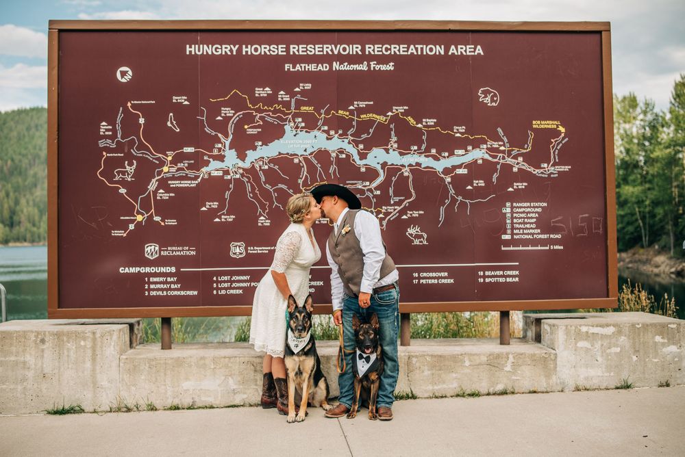 Couple with two dogs posing in front of Hungry Horse Reservoir Recreation Area sign in Flathead National Forest.