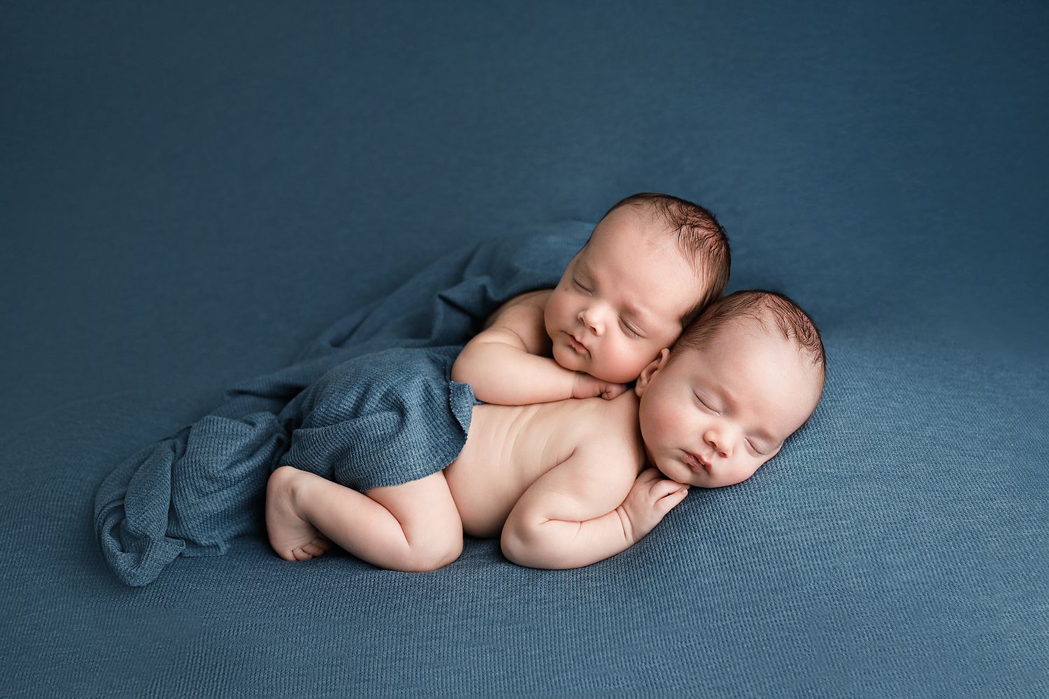 Two sleeping newborn twins cuddled together on a blue blanket in a peaceful newborn photography session. Utah County twin photographer