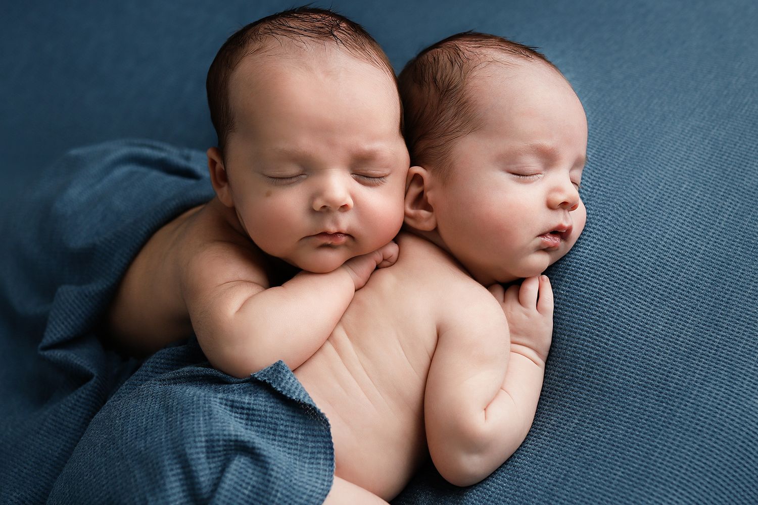 Two sleeping newborn twins cuddled together on a soft blue blanket in a peaceful studio photo. Utah County twin newborn photographer