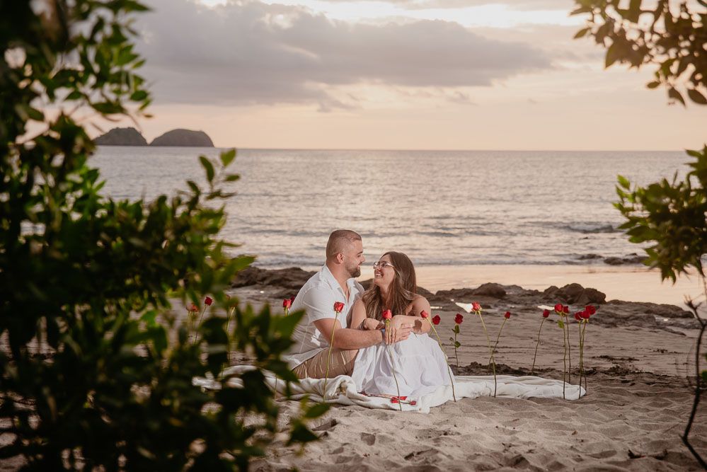 Surprise proposal moment captured on a beach with lush greenery background.