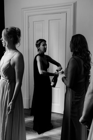 Documentary style photo of the mother of the bride in sweeping gown, opening a champagne bottle before a Milwaukee wedding ceremony.