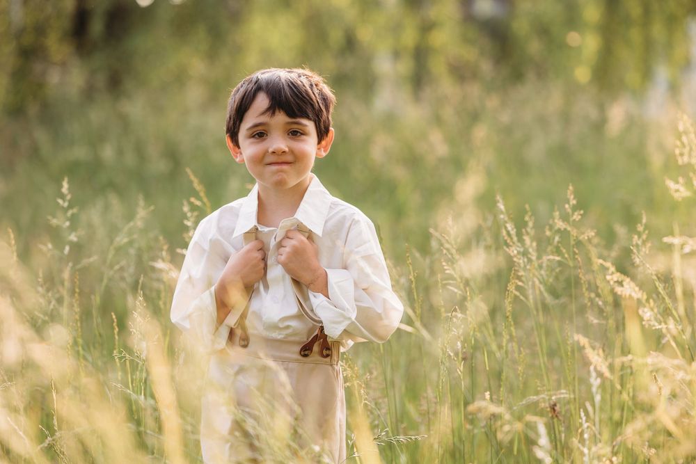 Young boy in white shirt standing in tall golden grass field, smiling outdoors in warm natural sunlight.