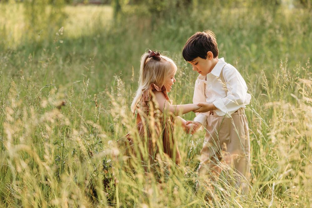 Two children playing together in a sunny field of tall green grass, a boy and girl sharing a sweet moment outdoors.