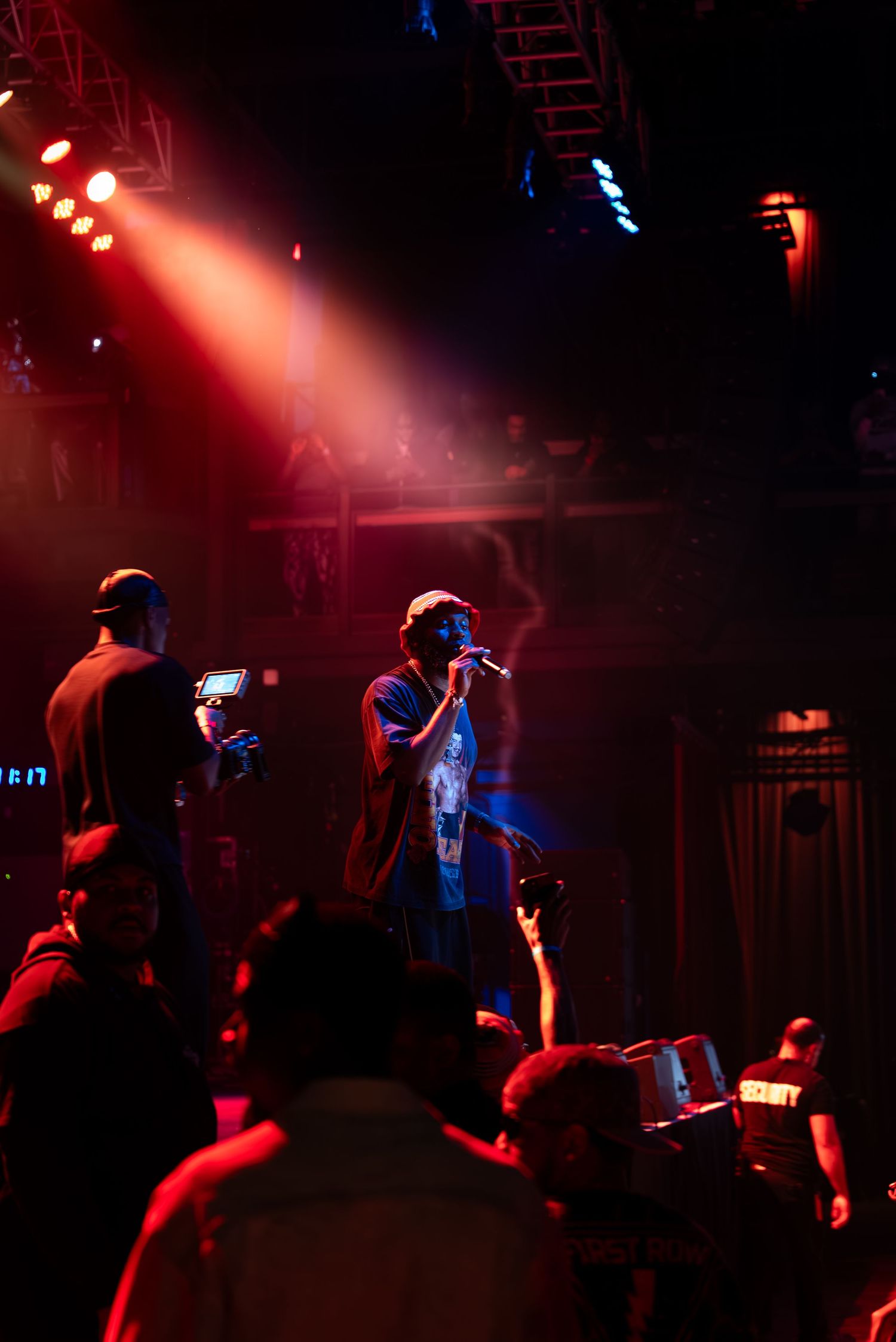 Concert performance in a dark venue with spotlights and crowd silhouettes.