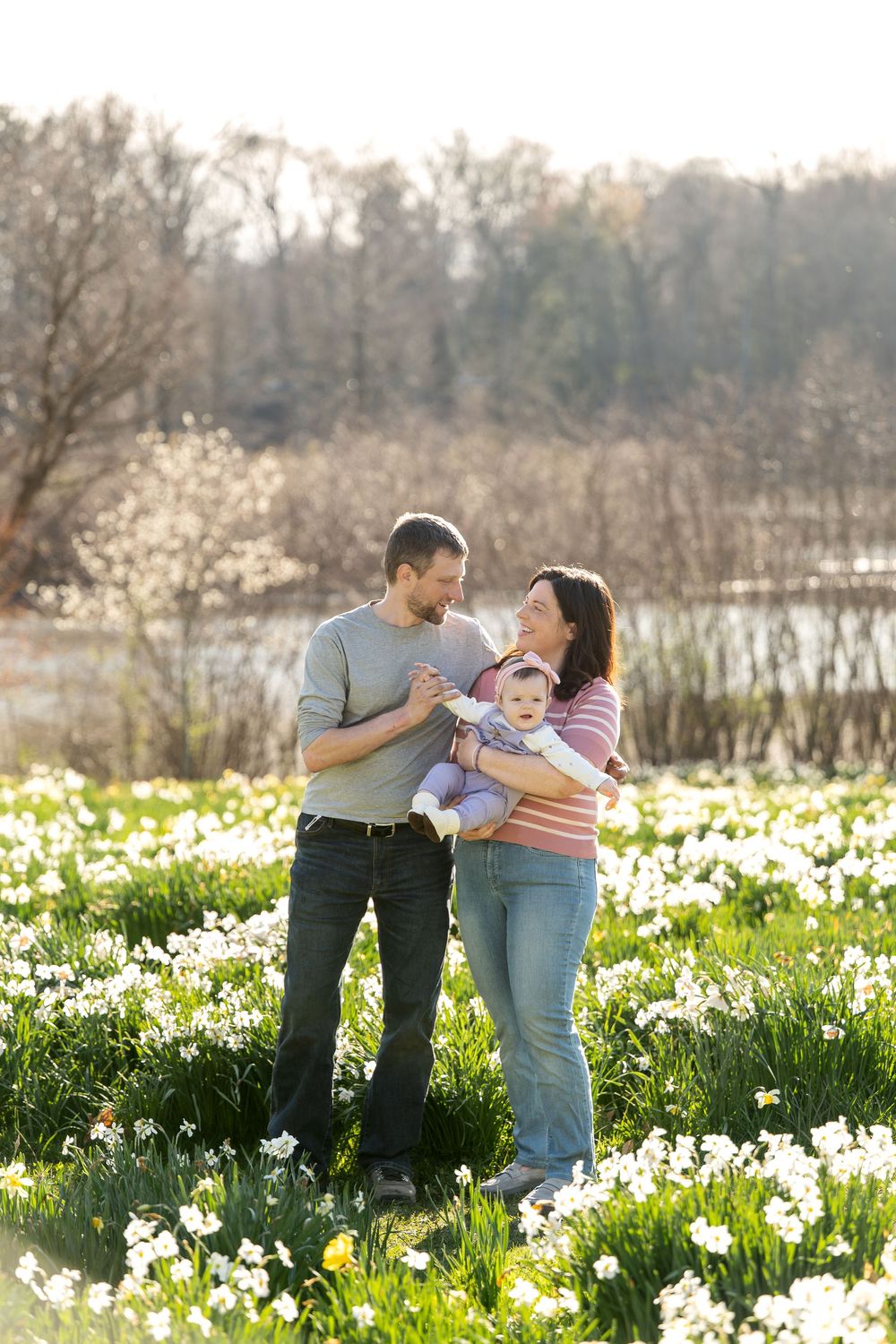 A happy young couple interacts lovingly with their baby in a gorgeous spring daffodil field outdoors.