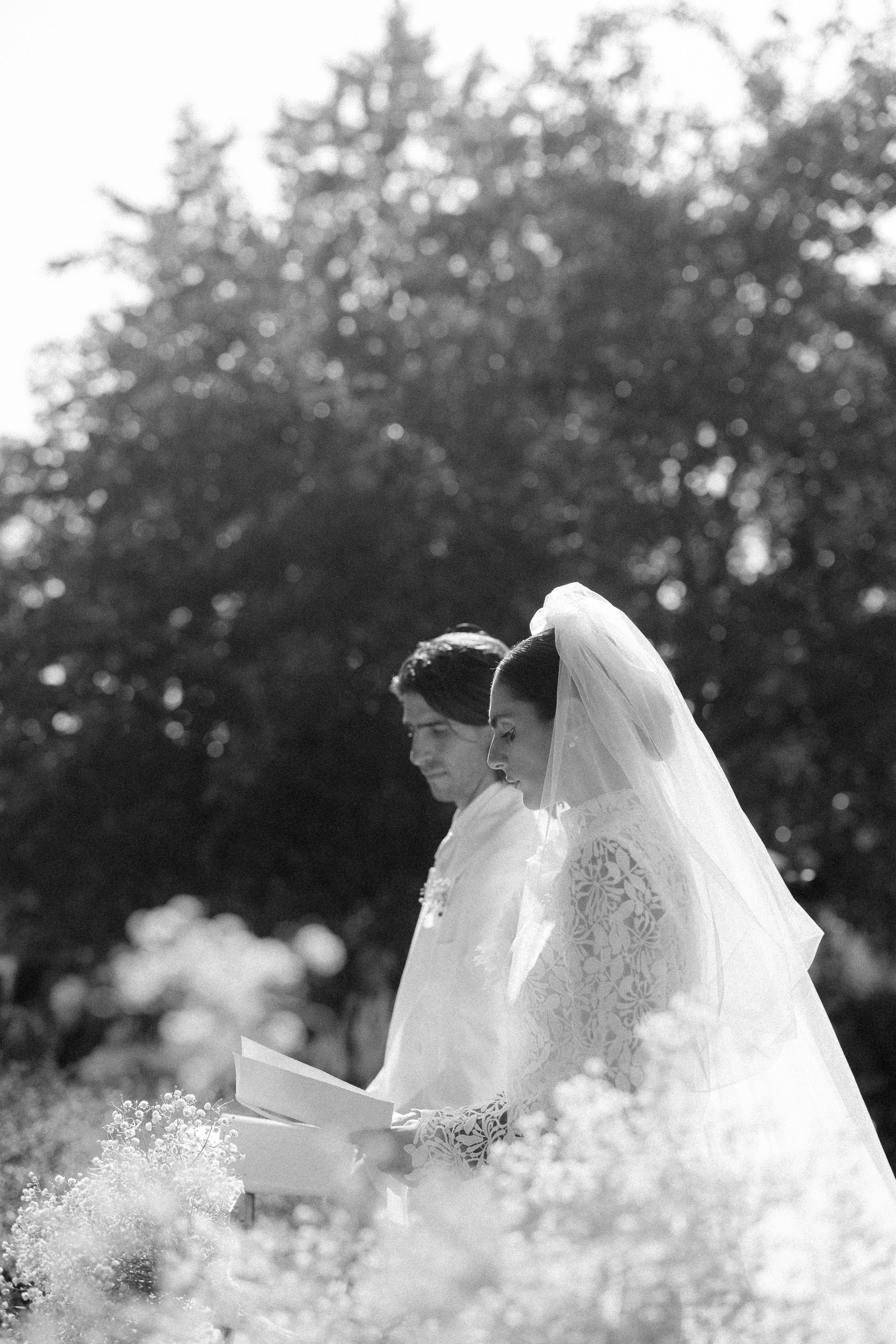Bride and groom exchange vows outdoors surrounded by wildflowers in elegant black and white wedding photo.