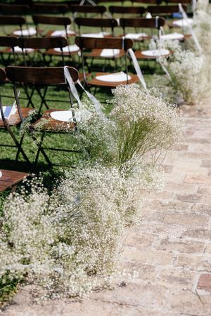 Elegant outdoor wedding ceremony aisle lined with delicate baby's breath flowers and wooden chairs.