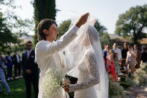 Groom lifts bride's veil during an outdoor wedding ceremony surrounded by guests.