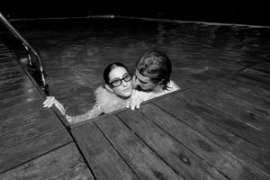 Couple sharing a romantic moment in a pool at night, woman wearing glasses, black and white photography.