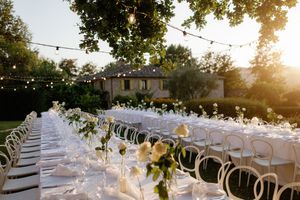 Elegant outdoor wedding reception with long tables, white florals, string lights, and golden sunset ambiance.