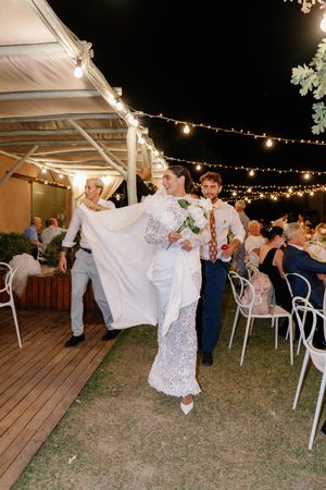 Bride and groom make grand entrance at outdoor evening wedding reception with string lights.