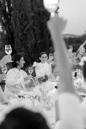 Guests raising wine glasses in a toast at an elegant outdoor wedding reception dinner in black and white.