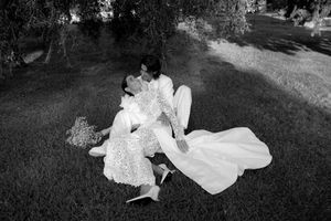 Black and white photo of newlyweds sharing a romantic kiss while sitting on grass.