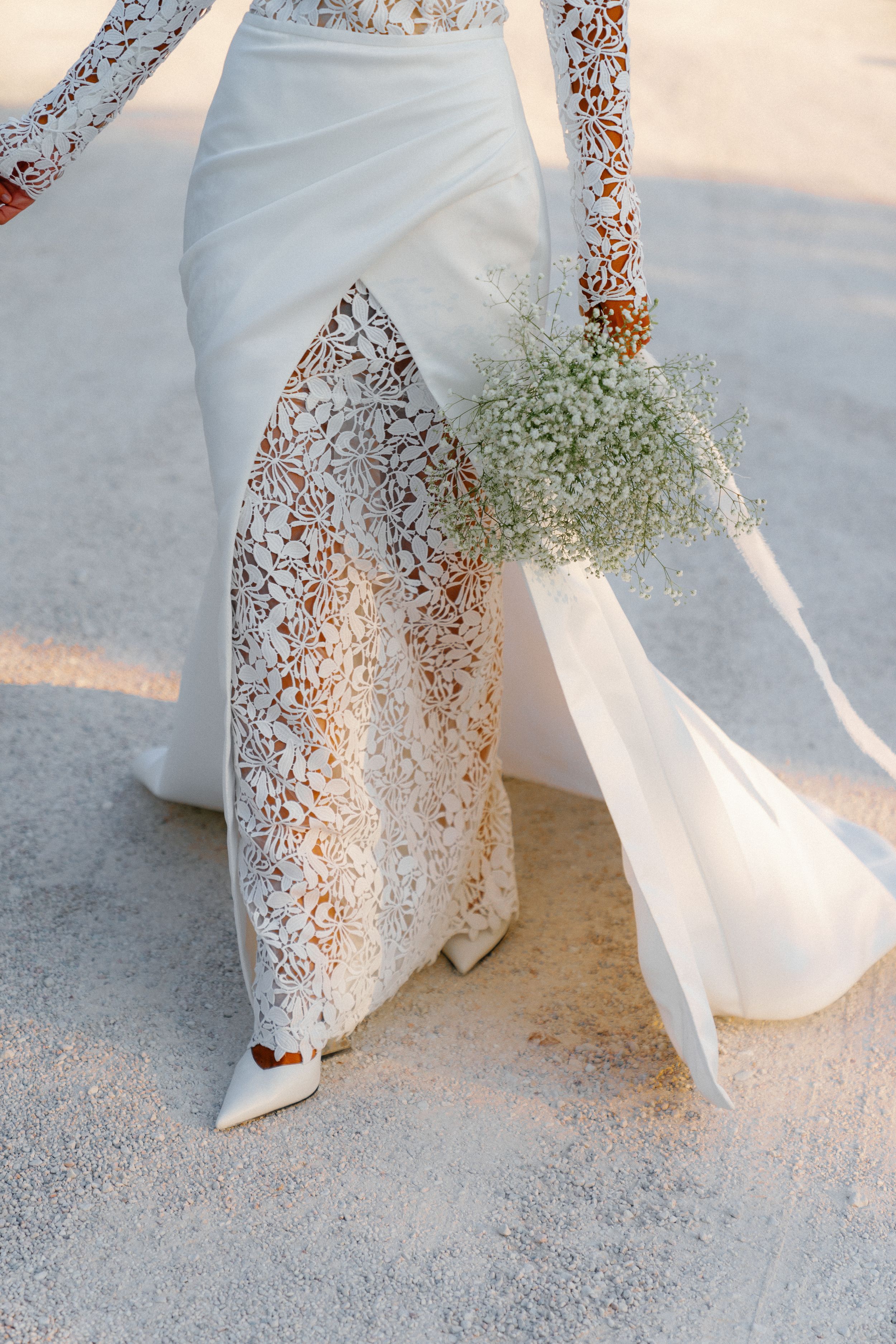 Bride in elegant lace and white gown walking with baby's breath bouquet, detail shot of dress train and heels.