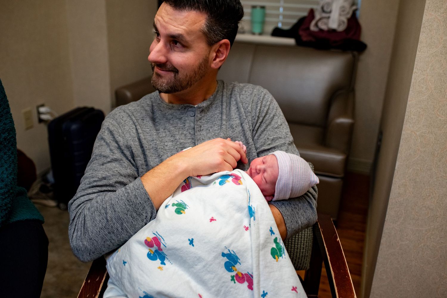 A person in a grey sweater holds a sleeping newborn wrapped in a butterfly-print blanket.