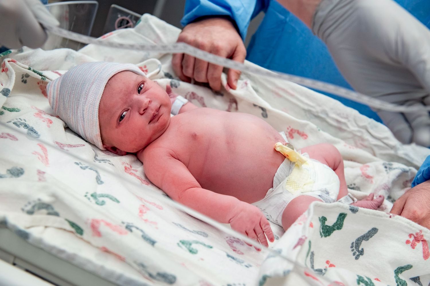 Newborn baby lying in hospital bassinet on patterned bedding.