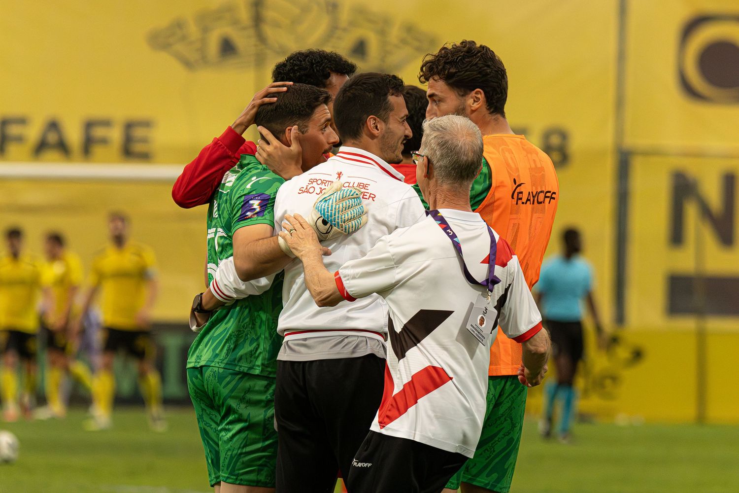 Soccer players in red and yellow jerseys compete for a header during an intense night match on a floodlit pitch.