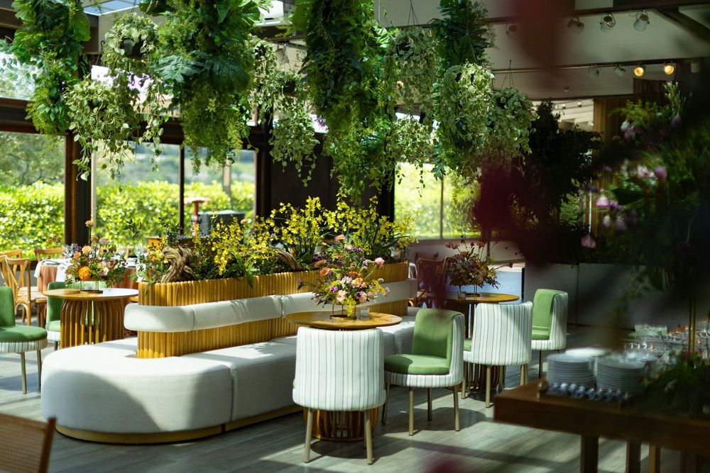 Luxurious greenhouse lounge featuring cascading plants, white curved seating, gold details, and vibrant floral arrangements.