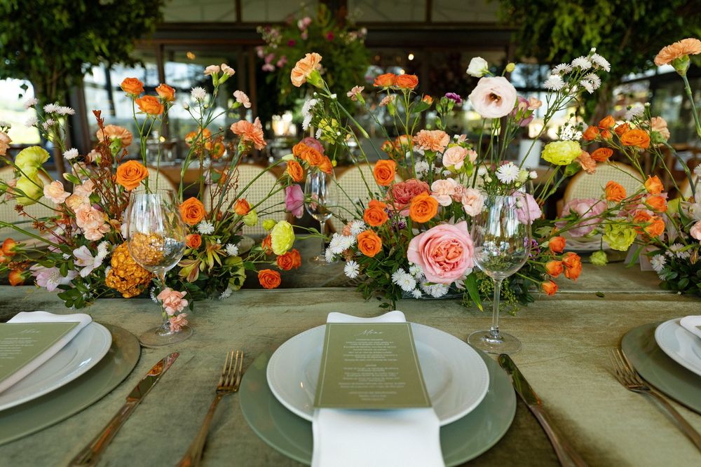 Elegant wedding reception table with lush orange, pink, and white floral centerpieces, gold cutlery, and green menu cards.