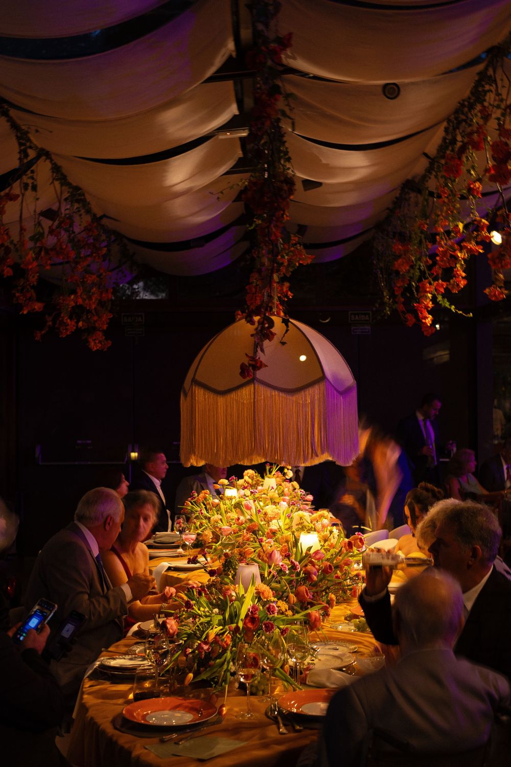 Elegant candlelit dinner party with floral centerpieces under draped ceiling with hanging flowers.