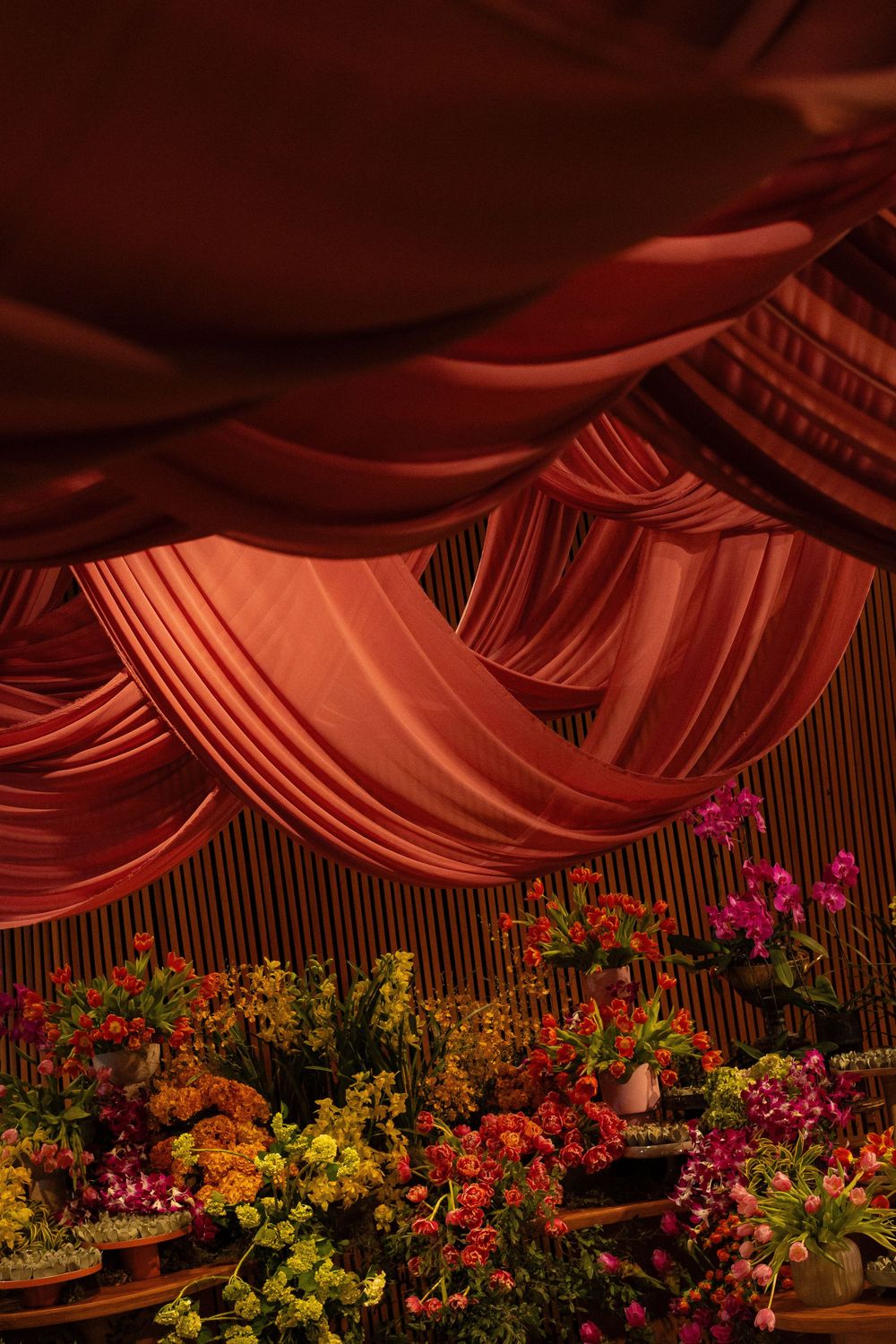 Elegant red draped fabric ceiling above colorful floral arrangements in warm tones at a decorated event venue.
