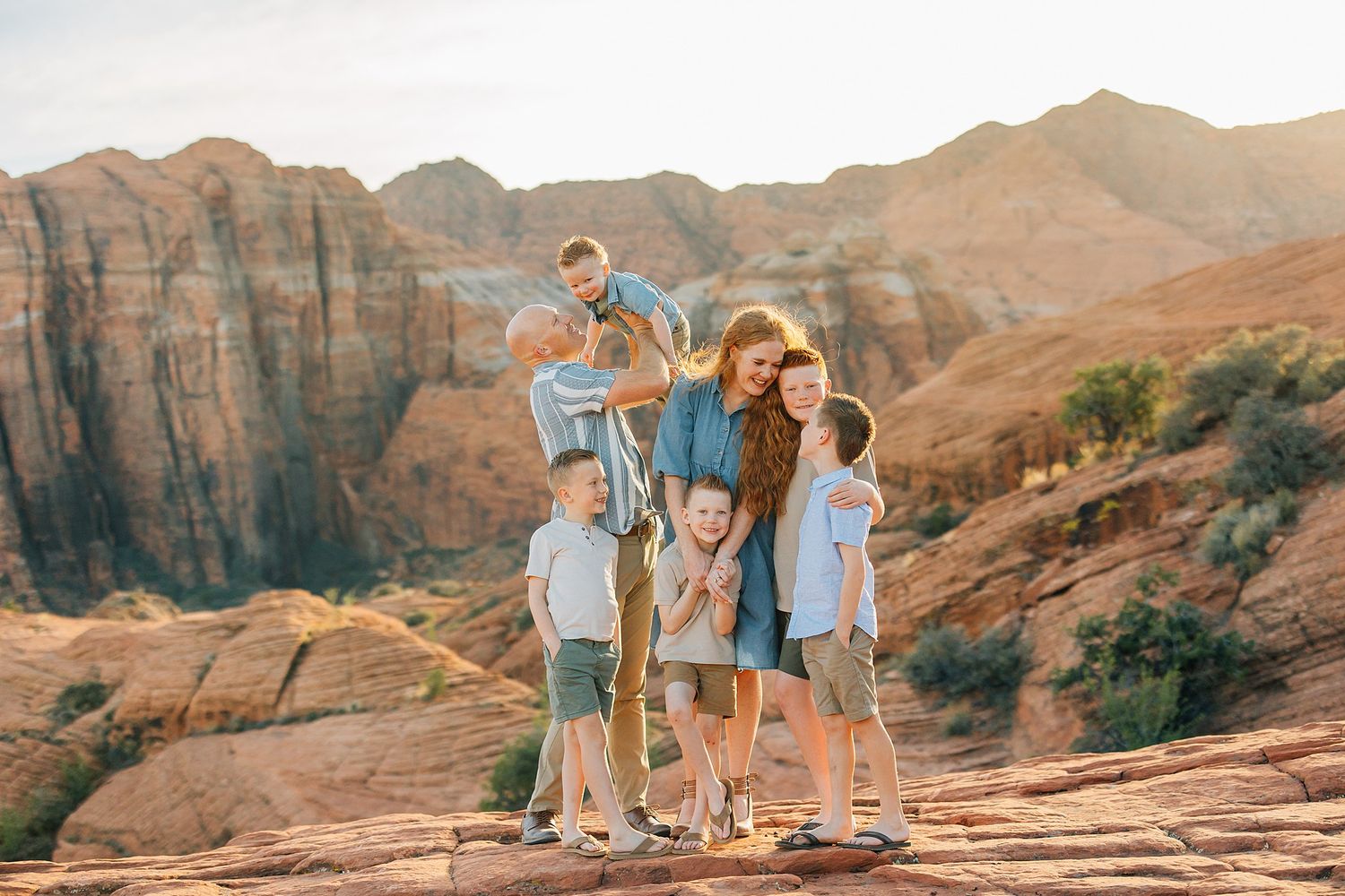 Family in teal outfits walking by a scenic lake with red rock mountains in the background at sunset.