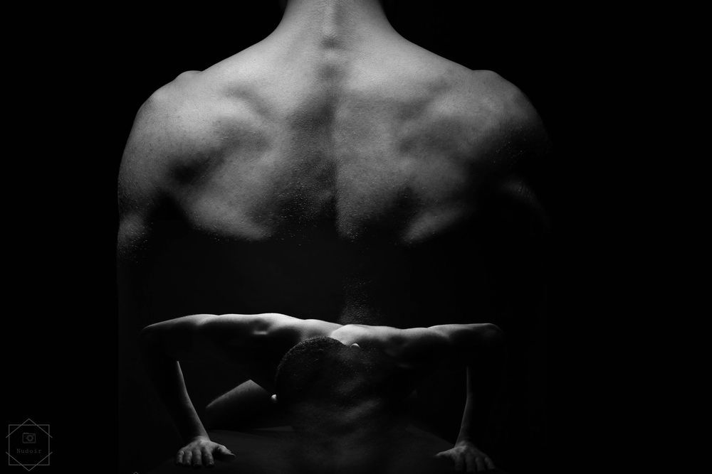 Black and white photo of a muscular male back showcasing defined muscles and athletic physique against dark background.