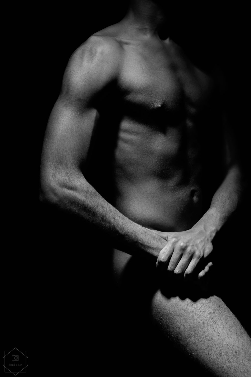 Black and white artistic photo of a muscular male torso with dramatic lighting highlighting defined abs and arms.