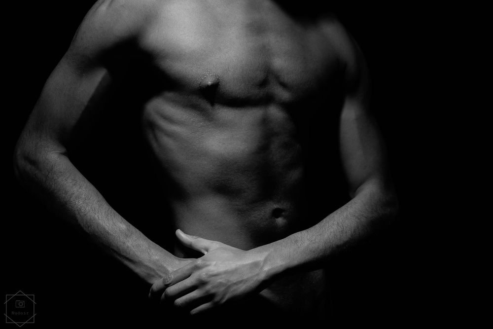 Black and white artistic photo of a fit male torso showing defined abs and muscles against dark background.