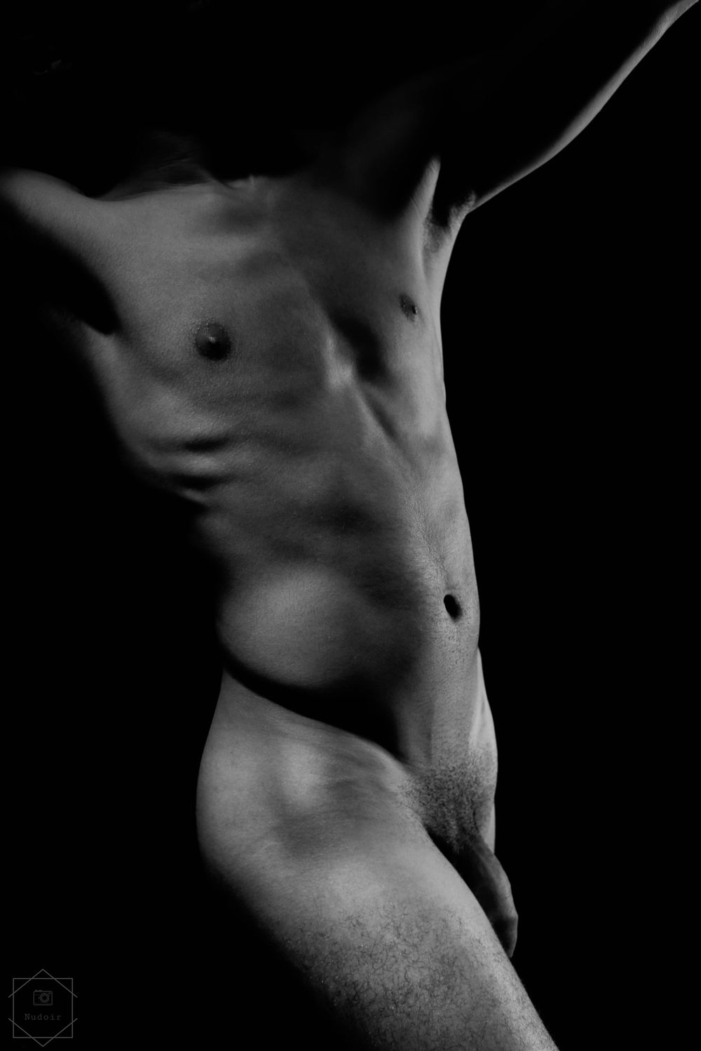 Black and white fine art nude male torso photograph with dramatic chiaroscuro lighting on athletic physique.