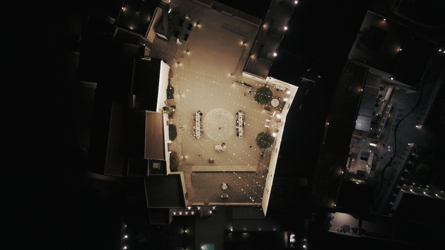 Aerial night view of an illuminated outdoor courtyard surrounded by dark buildings.