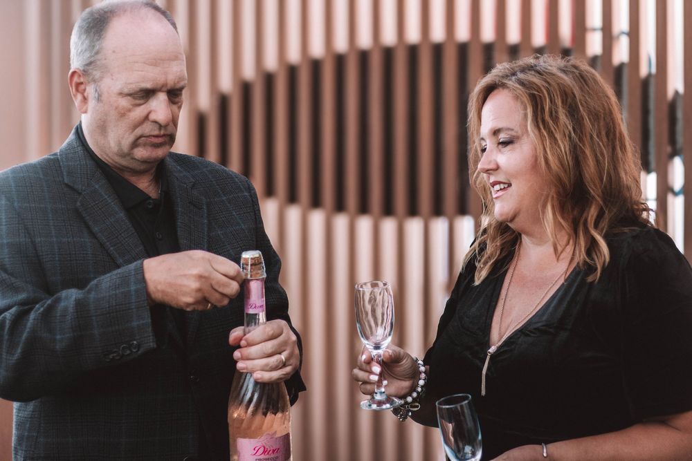 Couple sharing a romantic moment opening a pink bottle of champagne at an elegant indoor venue.
