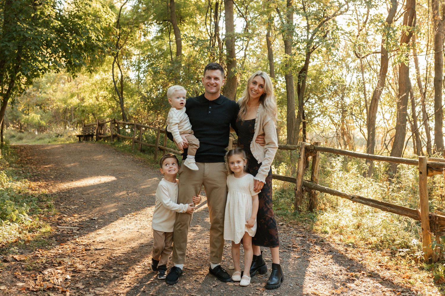 Happy family of five posing on wooded path in warm autumn sunlight.