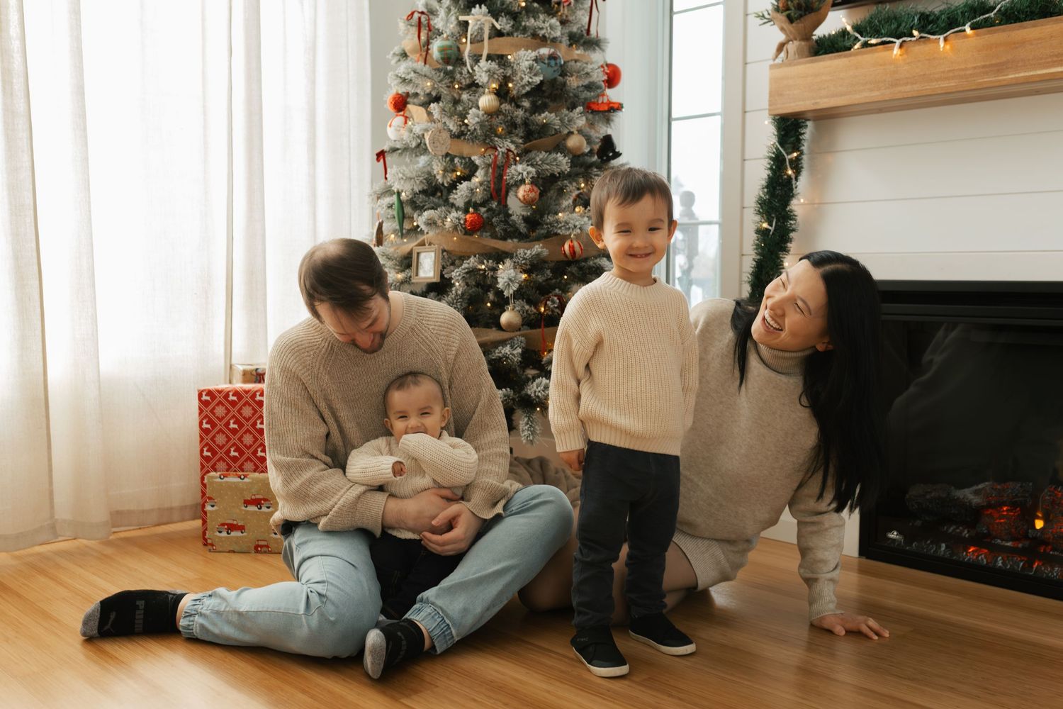 Happy Asian family with two young children celebrating Christmas near decorated tree and fireplace.